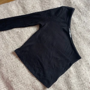 Svart ribbad oneshoulder topp - Säljer en svart ribbad topp med oneshoulder-design och lång ärm. Snygg och stilren modell som sitter tight