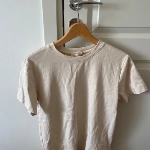Beige basic t-shirt i bomull - Enkel och stilren beige t-shirt i mjuk bomull. Klassisk rund halsringning och korta ärmar, perfekt för en clean och avslappnad look. Passar dig som gillar minimalistisk stil och neutrala färger.