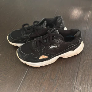 Svarta Adidas sneakers med chunky sula - Svarta Adidas sneakers med vit chunky sula och klassisk logga på sidan och hälen. Ovandelen är i mesh och mocka med snörning. Skorna har en sportig vibe och passar perfekt till streetwear eller casual outfits.