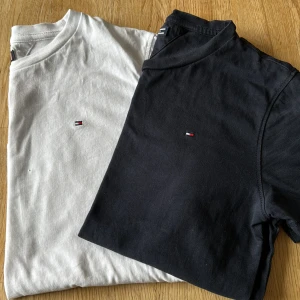 2-pack Tommy Hilfiger t-shirts, svart & vit - Två klassiska t-shirts från Tommy Hilfiger i storlek 152. En svart och en vit, båda med broderad logga på bröstet. T-shirtsen har rund hals och korta ärmar, tillverkade i mjuk bomull för en skön känsla. Perfekt basic med stilren design.