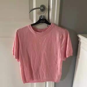Rosa stickad kortärmad tröja ONLY - Supersöt rosa stickad tröja från ONLY i storlek XL. Tröjan har korta ärmar, rund halsringning och ribbade kanter vid hals, ärmslut och nederkant. 