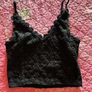 Svart spetsig croppad linnetopp H&M - Supersnygg svart croppad linnetopp från H&M med blommig spets och tunna axelband. Toppen har v-ringning och coola blommiga detaljer längs kanterna. Perfekt att styla med jeans eller kjol för en trendig look.