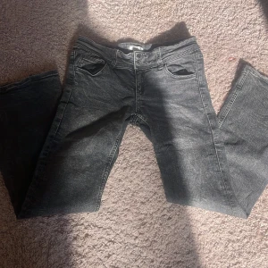 Svarta jeans från Gina Tricot, stl 152 - Snygga svarta jeans från Gina Tricot i storlek 152. Jeansen har klassisk femficksdesign, dubbla knappar i midjan och coola detaljer på bakfickorna. Materialet är slitstarkt denim med en tvättad look som ger en trendig vibe.