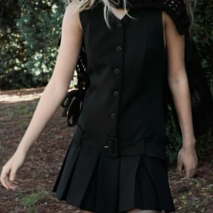 Svart ärmlös klänning med knappar och bälte - Snygg svart ärmlös klänning med knappar framtill och ett brett bälte i midjan. Skriv privat för fler bilder, men det sina ej några defekter och täcken på andvändning. 