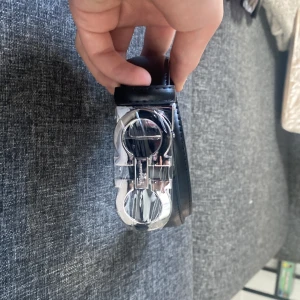 Svart bälte med silverfärgat spänne från Salvatore Ferragamo - Snyggt svart bälte i skinn med ett stort, blankt silverfärgat spänne i Ferragamos ikoniska design. Perfekt accessoar för att lyfta din outfit med en exklusiv touch. Beltrt är ett snyggt moosnuckels bälte som passar med nästan allt helt nytt avdrig använt 