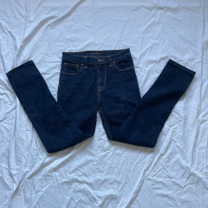 (HELT NYA) utan prislapp mörkblå Nudie jeans - Säljer ett par mörkblå jeans från Nudie Jeans med klassisk femficksdesign och orangea sömmar. Pris kan diskuteras vid köp! + nyskick utan prislapp