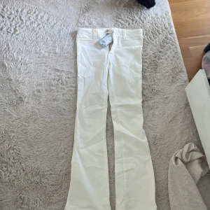 Vita bootcut jeansbyxor från H&M - Säljer ett par vita bootcut jeansbyxor från H&M i storlek 164. Byxorna har klassisk femficksdesign, bälteshällor och stängs med dragkedja och knapp. Perfekta för dig som gillar en stilren look med lite utsvängda ben.