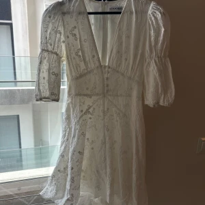 Vit blommig klänning från Adoore - Superfin vit klänning från Adoore med blommigt mönster och v-ringning. Klänningen har trekvartsärm och lätt volang nertill. Perfekt för sommarens alla tillfällen!