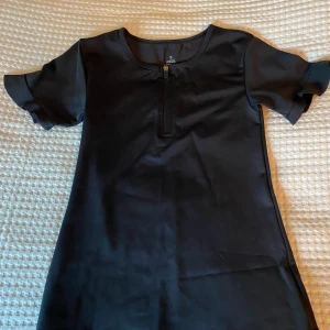 Svart sportig top från aim'n - Svart kortärmad top från aim'n med dragkedja framtill samt med en lite volang på ärmarna. Tillverkad i stretchigt material med 73% polyester och 27% spandex. Enkel och stilren design, perfekt för en aktiv livsstil.