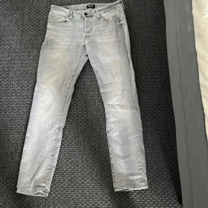 Jack & Jones jeans - Säljer ett par ljusgrå jeans med slim passform. Klassisk femficksmodell. Jeansen har raka ben och är perfekta för en stilren vardagslook.