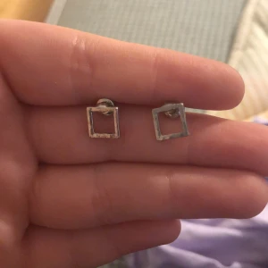 Silvriga fyrkantiga örhängen - Säljer ett par minimalistiska örhängen i silverfärgad metall med öppen fyrkantig design. Perfekta för dig som gillar stilrena och enkla smycken. Stiftmodell som är lätta att bära till vardags.