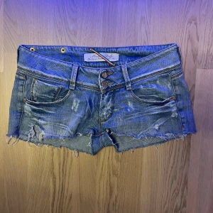 Blå jeansshorts från MET - Säljer ett par blå jeansshorts från MET med slitna detaljer och fransig kant. Super snygga med låg midja och slitna kanter. Super snygga till sommaren. Storlek w28