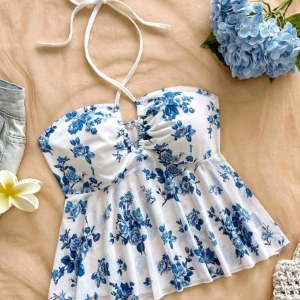 Vit och blå blommig halterneck topp - Supersöt topp med halterneck och blommigt blått mönster på vit botten. Lätt utsvängd nertill och med en liten v-ringning framtill. Aldrig använd💙☀️