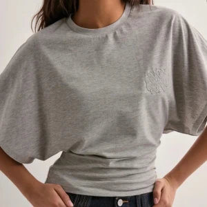 Grå top - Säljer en stilren grå top med rund hals och korta ärmar. Topen har en diskret broderad logga på bröstet och är tillverkad i mjuk bomull. Aldrig använd 