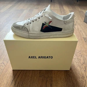 Vita sneakers från Axel Arigato - Säljer ett par vita sneakers från Axel Arigato. Skorna har snörning, rund tå och platt sula. Perfekta för dig som gillar stilrena och trendiga sneakers.