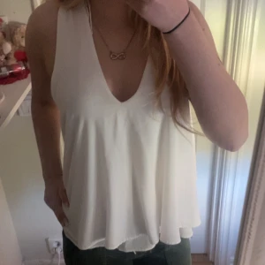 Vit satinlinnetopp med knappar i ryggen - Säljer en vit linnetopp i satin med djup v-ringning och breda axelband. Toppen har en lös passform och dekorativa knappar längs ryggen. Perfekt för sommardagar eller när du vill känna dig extra fin.