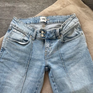 Ljusblå lågmidjade bootcut jeans från 157 - Säljer ett par ljusblå jeans från 157 med bootcut-passform och hög midja. Jeansen har synliga sömmar framtill, dubbla knappar och klassiska fickor både fram och bak. Perfekta för dig som gillar en retroinspirerad look.
