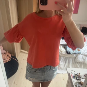 Korallfärgad topp med volangärmar - Säljer en korallfärgad topp med rund halsringning och korta volangärmar. 