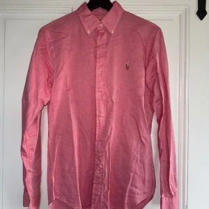Rosa skjorta från Ralph Lauren - Klassisk rosa oxfordskjorta från Ralph Lauren med button-down krage. Använd vid 2 tillfällen. Som ny.