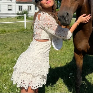 MAJE klänning - Superfin vit kortklänning med broderad spets, volanger och cut-out detaljer i midjan. Klänningen har trekvartsärmar med puff och rund halsringning. Perfekt för sommarens alla tillfällen!