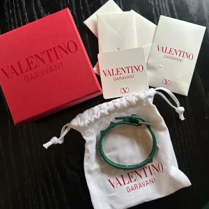 Grönt armband med nitar från Valentino Garavani - Säljer ett grönt armband från Valentino Garavani med silverfärgade pyramidformade nitar. Armbandet är i läder och har ett justerbart spänne. Kommer med originalförpackning och dustbag.