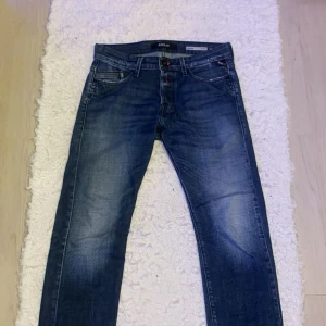 Blå Replay Waitom jeans - Säljer ett par klassiska blå jeans från Replay, modell Waitom Regular Fit. Jeansen har fem fickor, snygga slitningar och raka ben. Perfekta för dig som gillar en tidlös stil med bekväm passform. Storlek W29 L32