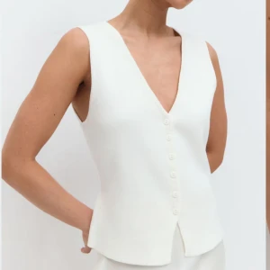Vit v-ringad väst med knappar - Stilren vit väst med v-ringning och knäppning framtill. Västen har en rak passform och ger en modern och fräsch look. Går lika bra till en shoppingdag på stan till en utekväll med vännerna. Ett tidlöst plagg som aldrig går ur tiden! 