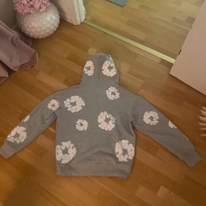 Denim tears hoodie - Säljer en grå Denim Tears hoodie med vita blommönster över hela tröjan. Den har en klassisk huva och långa ärmar, perfekt för en avslappnad stil. Passar bra till både jeans och joggers. Pris kan diskuteras:)