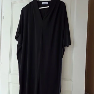 Svart långklänning från Wera - En svart långklänning från Wera med v-ringad hals och lös passform. Klänningen har korta ärmar och ett minimalistiskt, stilrent uttryck. Perfekt för dig som gillar enkel och tidlös design. Priset går alltid att diskutera!