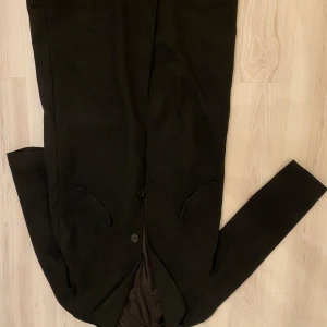 Svart kappa från H&M Divided - Säljer en lång svart kappa från H&M Divided i storlek XS. Klassisk rak modell med knäppning framtill och två fickor. Perfekt för dig som gillar stilrena och tidlösa plagg.