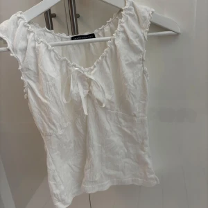 Söt sommartopp från brandy Melville  - Söt vit topp med knytning framtill. Toppen har en lätt rynkad struktur.. Perfekt för varma dagar och enkel att matcha med jeans eller kjol.
