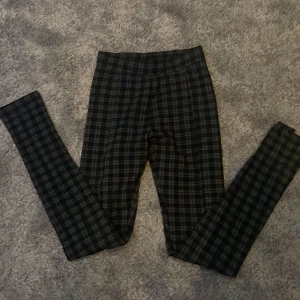 Svarta och gråa rutiga leggings från H&M - Snygga leggings från H&M i svart och grått med rutig design. Byxorna har en tight passform och är tillverkade i ett stretchigt syntetmaterial som sitter bekvämt. Perfekta för dig som gillar mönstrade byxor med stilren känsla.