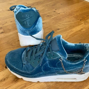 Blå Nike Air Max i sammet - Unika Nike Air Max sneakers i blå sammet med vita sulor och snygga kedjedetaljer på sidan.(avtagbara) Skorna har klassisk snörning och rund tå, vilket ger en modern och cool look. Perfekta för dig som vill sticka ut med din stil.