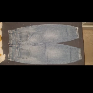 Blå jeansbyxor från Zara - Säljer ett par klassiska blå jeans från Zara med hög midja och raka ben. Jeansen har slitna detaljer framtill och fem fickor. Perfekta för en avslappnad och trendig look.