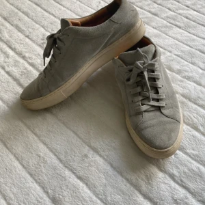 Gråa Polo Ralph Lauren i mocka - Säljer ett par stilrena grå sneakers från Polo Ralph Lauren i mjuk mocka. Skorna har snörning, rund tå och en ljus sula. Insidan är fodrad i beige och märket syns både på hälen och sulan. Perfekta för en clean och avslappnad look.