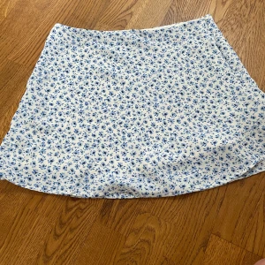 Vit och blå blommig kjol från H&M Divided - Supersöt vit kjol med blått blommönster från H&M Divided. Kjolen har en kort passform och är perfekt för varma dagar. Lätt och luftig känsla, passar till många olika stilar.