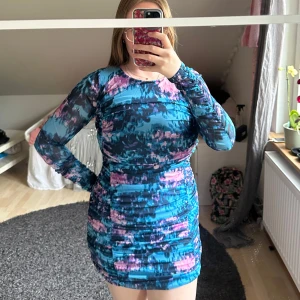 Blå och rosa mönstrad långärmad kortklänning - Säljer en tight kortklänning med blått och rosa abstrakt mönster. Klänningen har långa ärmar och figurnära passform, perfekt för dig som gillar färg och vill sticka ut. Materialet känns stretchigt och bekvämt.