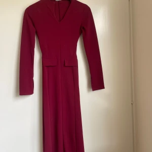 Vinröd långklänning  - Säljer en elegant vinröd långklänning med v-ringad hals och långa ärmar. Klänningen har en figurnära passform och stilrena detaljer vid midjan. Från ASOS, använd två gånger.