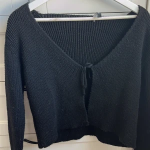 Svart stickad kofta från Trendyol - Säljer en svart stickad kofta från Trendyol i storlek M. Koftan har långa ärmar, v-ringning och knytning framtill. Perfekt för lager-på-lager och enkel att matcha med olika outfits. Snörrningen är lite sönder men inget som märks vid användning. 