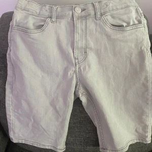 Ljusgrå jeansshorts från H&M - Säljer ett par ljusgrå jeansshorts från H&M med klassisk femficksdesign och knappgylf. Shortsen har normal passform och är perfekta för varma dagar. Stilrena och enkla att matcha med olika outfits.