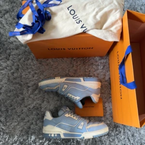 Louis Vuitton sneakers i ljusblått och vitt trainers skor - Säljer ett par Louis Vuitton sneakers i ljusblått och vitt med vita snören och detaljer. Skorna har en sportig design med rund tå och platt sula. Kommer med originalkartong, dustbag och påse.