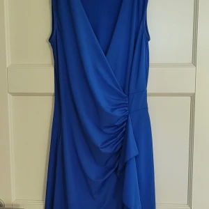 Smickrande kornblå omlottklänning NY! - Snygg blå omlottklänning från Anna Field med draperad detalj i midjan. V-ringad med smickrande rynkdetaljer och liten volang nedtill fram. Aldrig använd, nyskick! 38, sitter som ett smäck, tyvärr för liten för mig (40-42) Bra strechigt tyg med fint fall. Fler bilder finns.