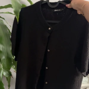 Svart kofta från Gina Tricot - En klassisk svart kofta från Gina Tricot med rund halsringning och knappar framtill. Perfekt att slänga över en topp eller klänning. Enkel och stilren design som passar till det mesta. Används inte