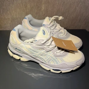 Vita och ljusblå sneakers från Asics - Säljer ett par fräscha vita och ljusblå sneakers från Asics med mesh- och syntetpaneler. Skorna har snörning, rund tå och en platt sula. Perfekta för dig som gillar sportig stil och vill ha bekväma skor till vardagen.