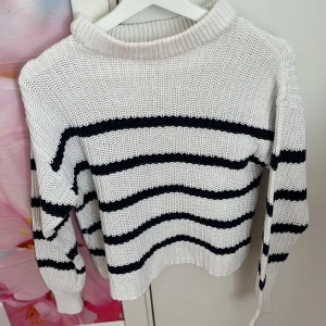 Vit och svart randig stickad tröja från 157 - Säljer en vit stickad tröja från 157 med svarta horisontella ränder. Tröjan har en bred ribbad krage och långa ärmar med ribbade muddar. Perfekt för kyligare dagar och enkel att matcha med jeans eller kjol.