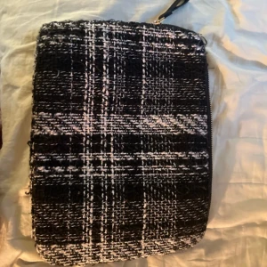 Svartvit rutig kuvertväska från Wera - Säljer en svartvit rutig kuvertväska från Wera. Väskan har ett grovt vävt tyg i svart och vitt med dragkedja upptill. Perfekt för att bära det viktigaste och ge din outfit en cool touch.