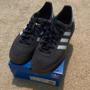 Adidas Handball Spezial sneakers - Mörkblå Adidas Handball Spezial sneakers med klassiska ljus blå  ränder på sidorna och brun gummisula. Skorna har snörning och är tillverkade i mocka.