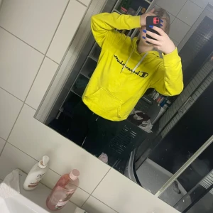 Gul hoodie från Champion - Säljer en gul hoodie från Champion i storlek small. Tröjan har huva, magficka och svart logga framtill. Perfekt för dig som gillar färgglada och bekväma plagg. Snygg och enkel att matcha med jeans eller mjukisbyxor.