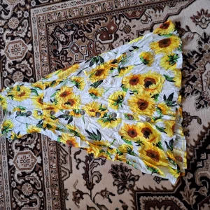 Vit klänning med solrosor och knappar - Säljer en somrig vit klänning med stora gula solrosor och gröna blad. Klänningen har knappar framtill och smala axelband. Perfekt för varma dagar och har en luftig, flowy passform.