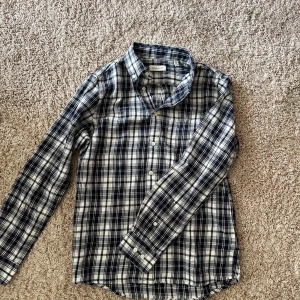 Rutig skjorta från GANT - Säljer en klassisk rutig skjorta från GANT i blått och vitt. Skjortan har lång ärm, knappar framtill och i mjuk flanell. Perfekt för dig som gillar en tidlös och stilren look.